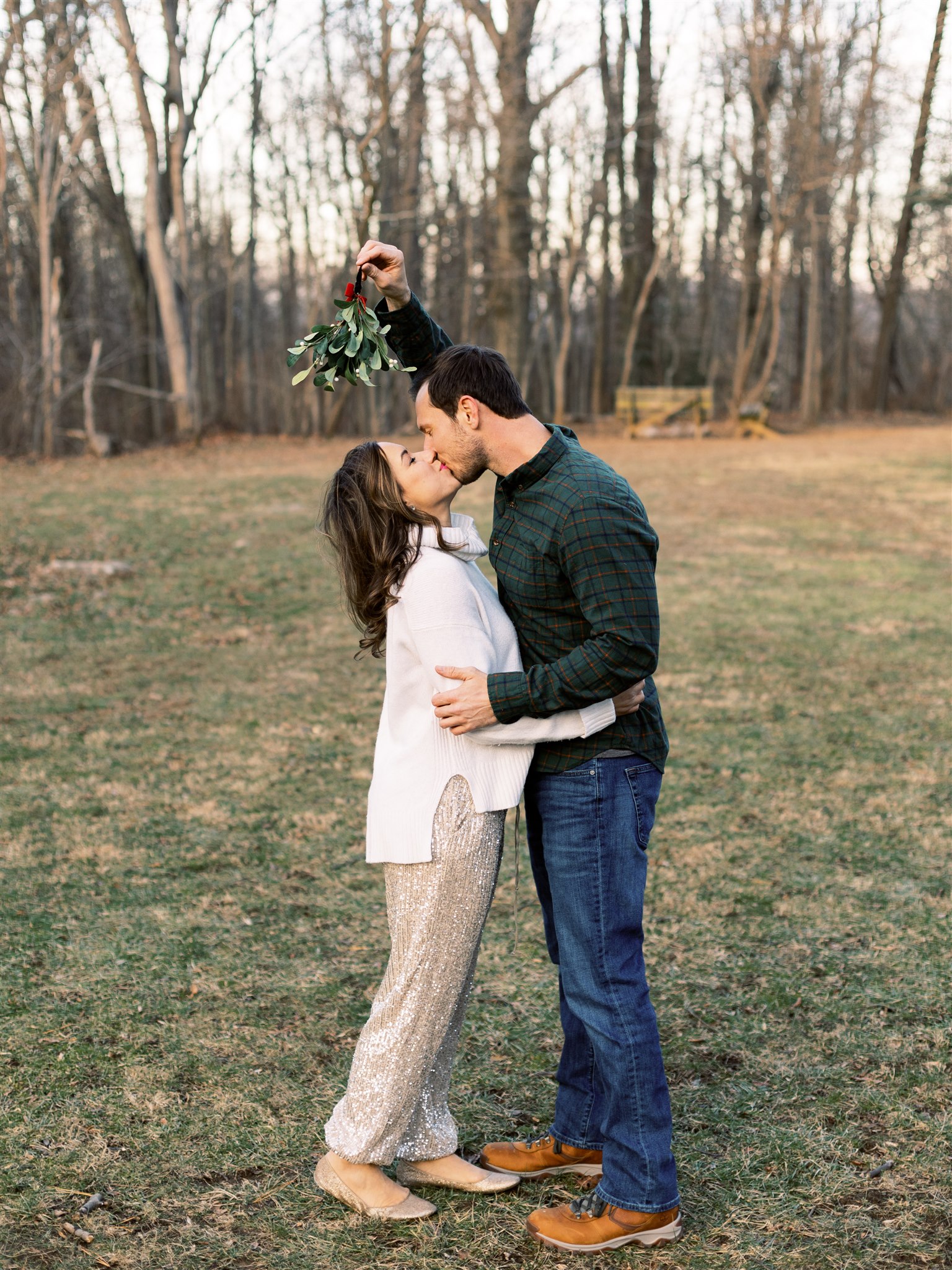 groom holds mistletoe for bride to kiss under