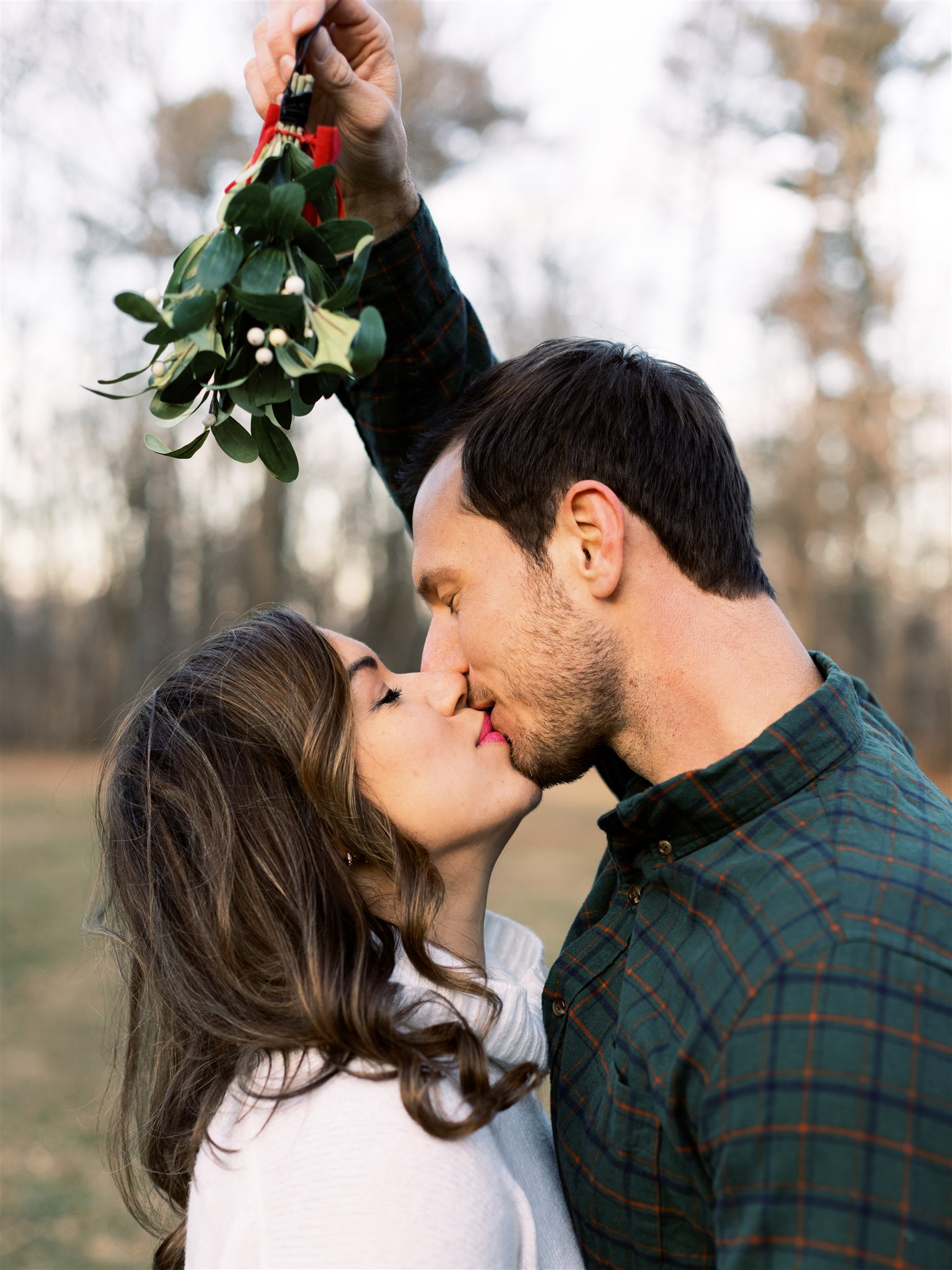 engaged couple kisses under mistletoe during winter engagement session