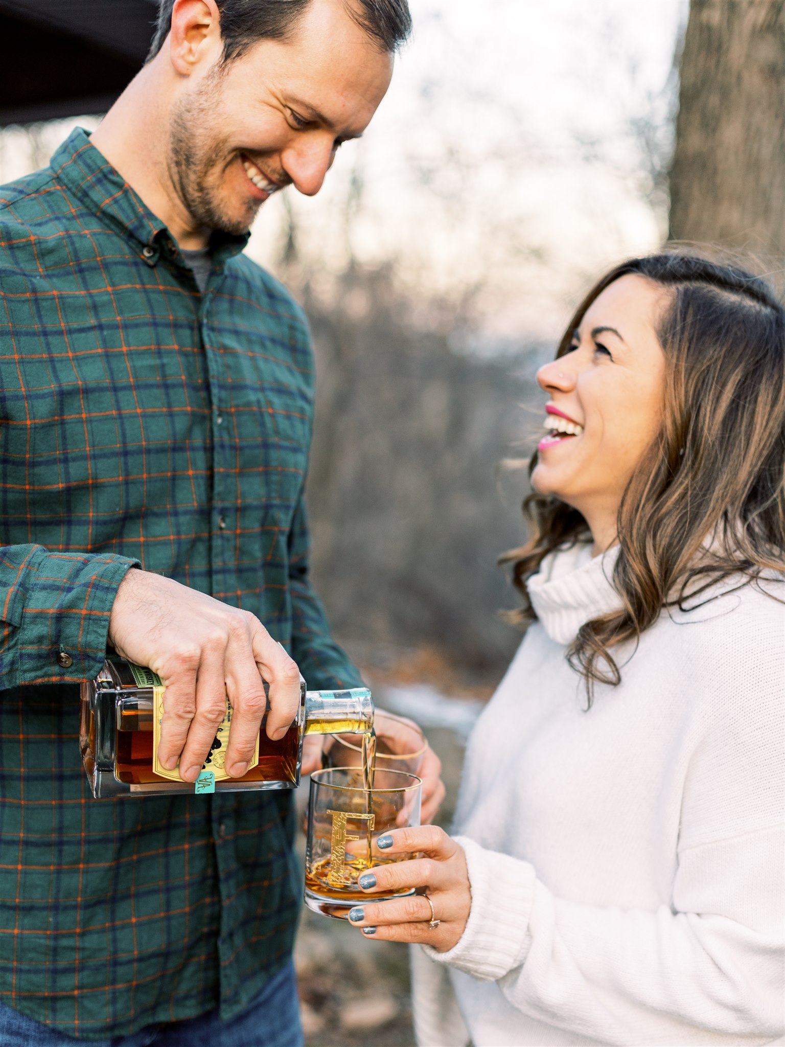 groom pours whiskey for bride during winter engagement session