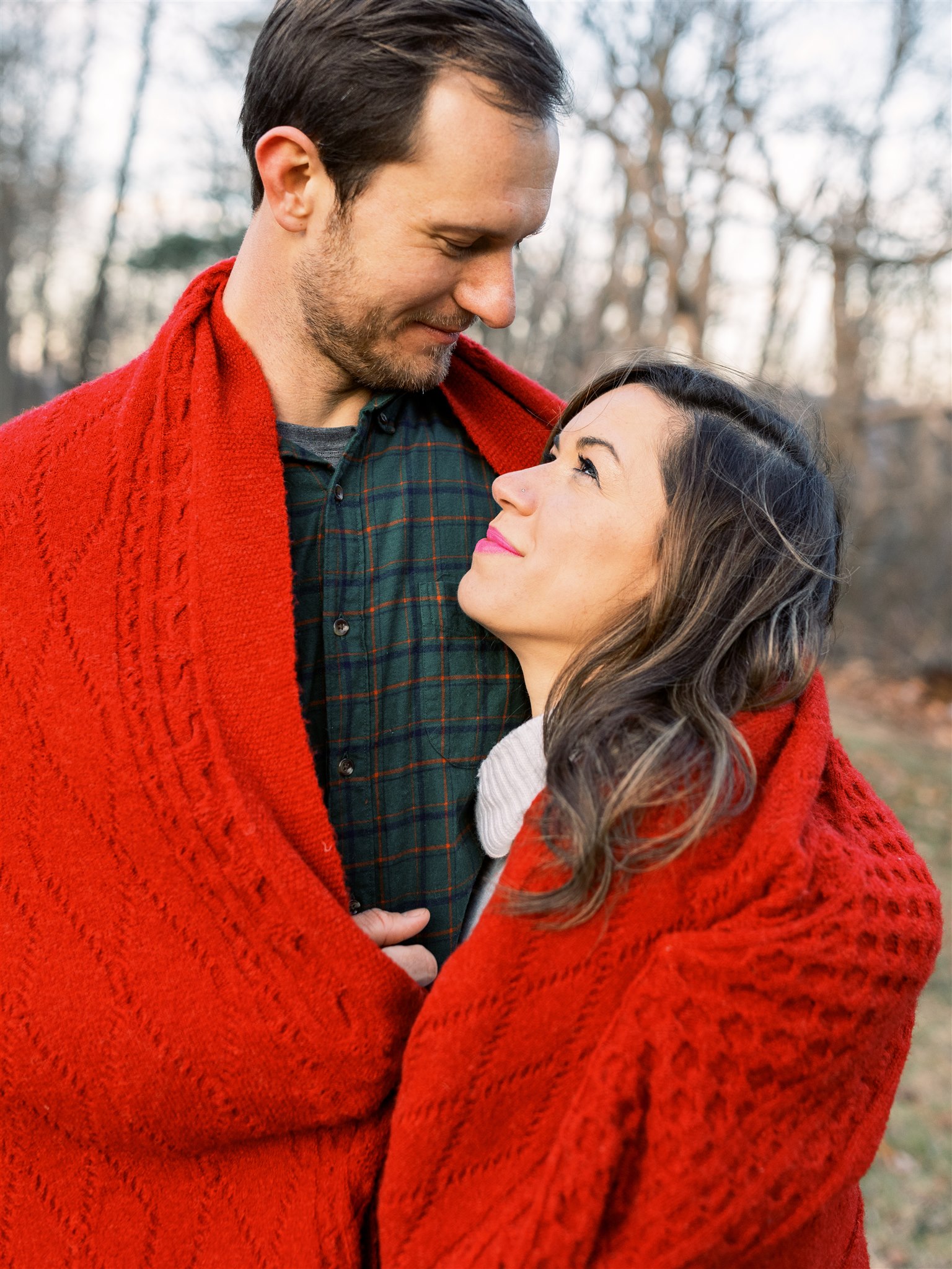 bride and groom stand together in red blanket