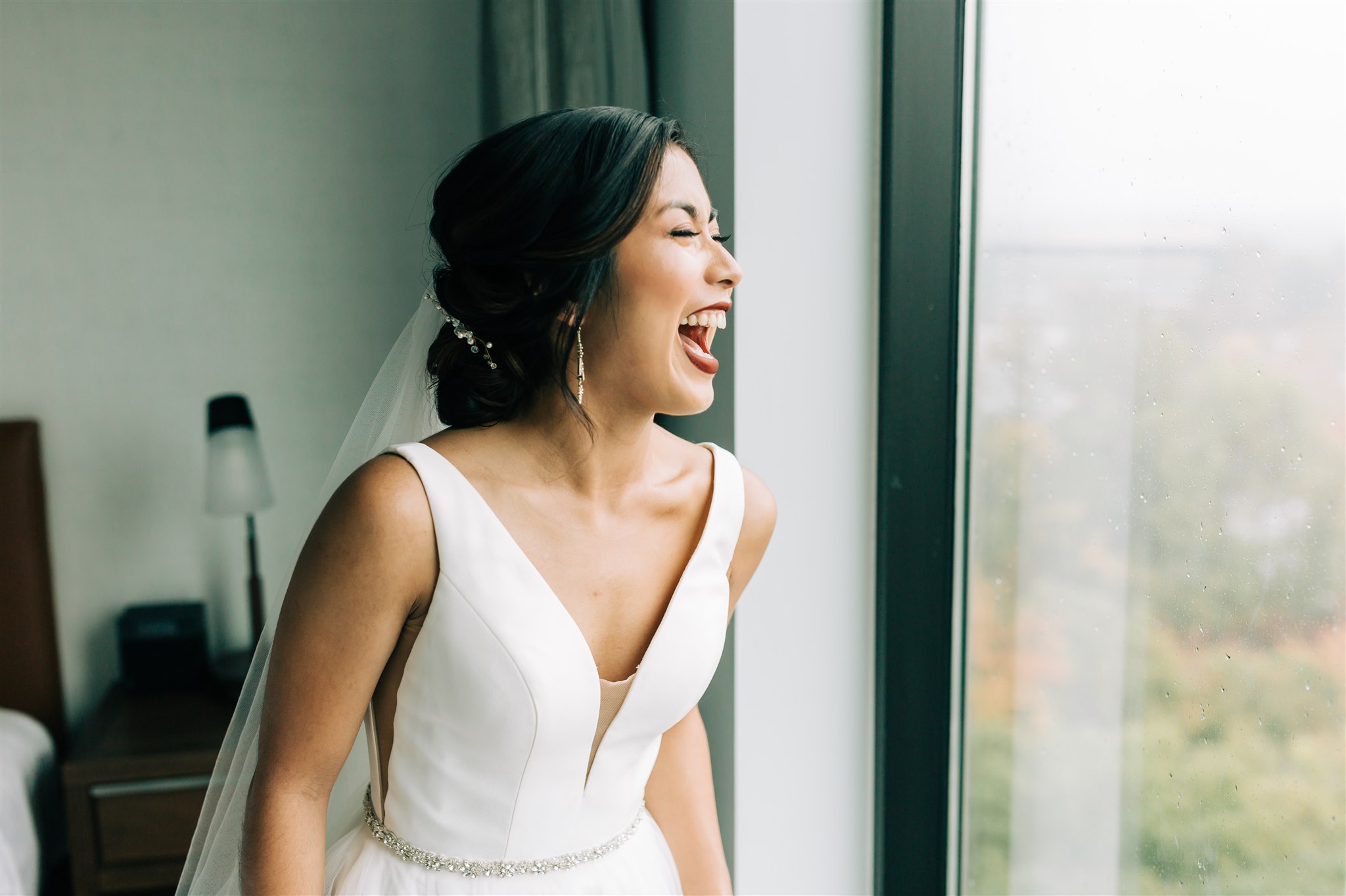 bride laughs looking out hotel window