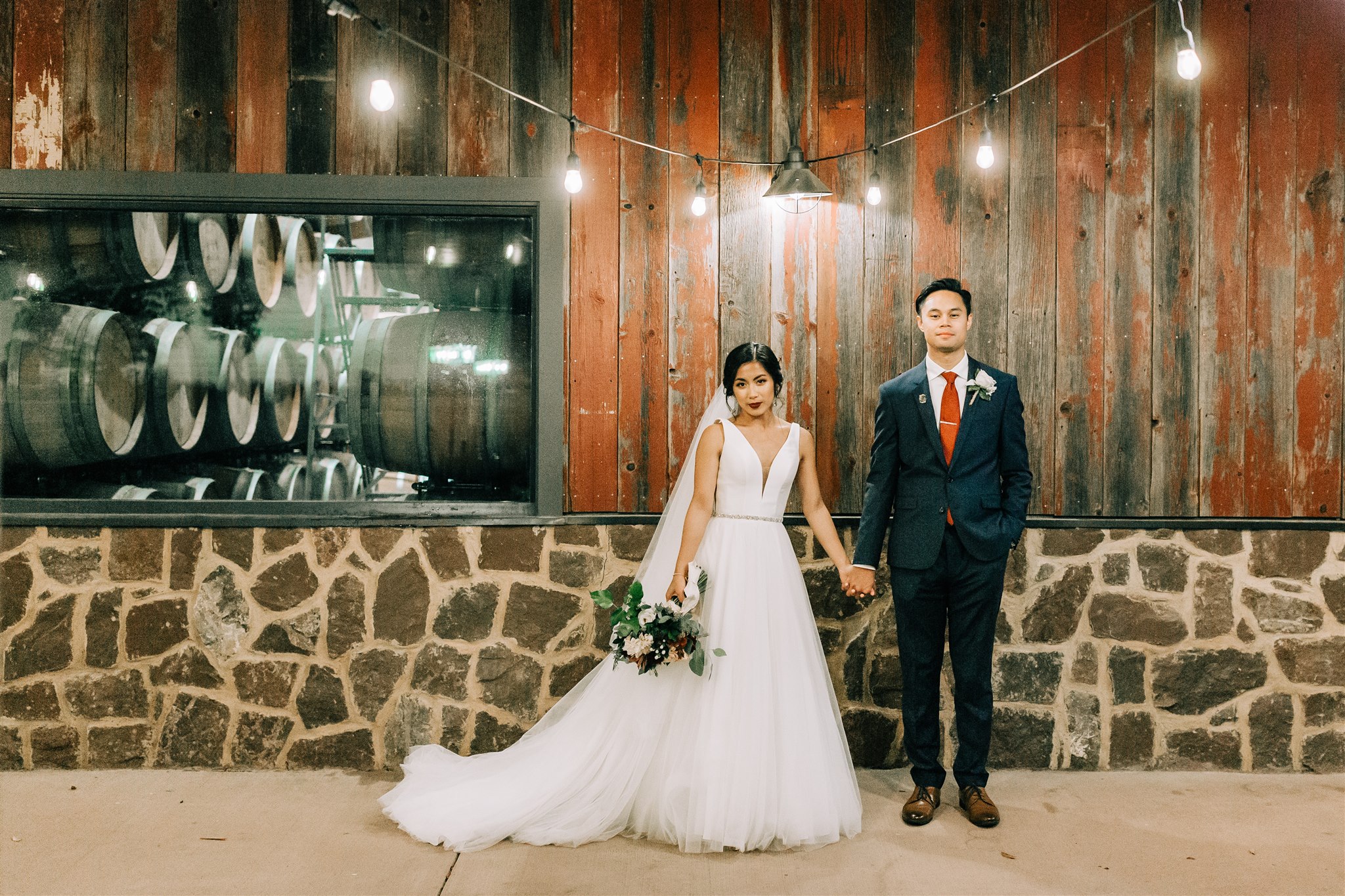 bride and groom hold hands posing by wood wall at Winery at Bull Run