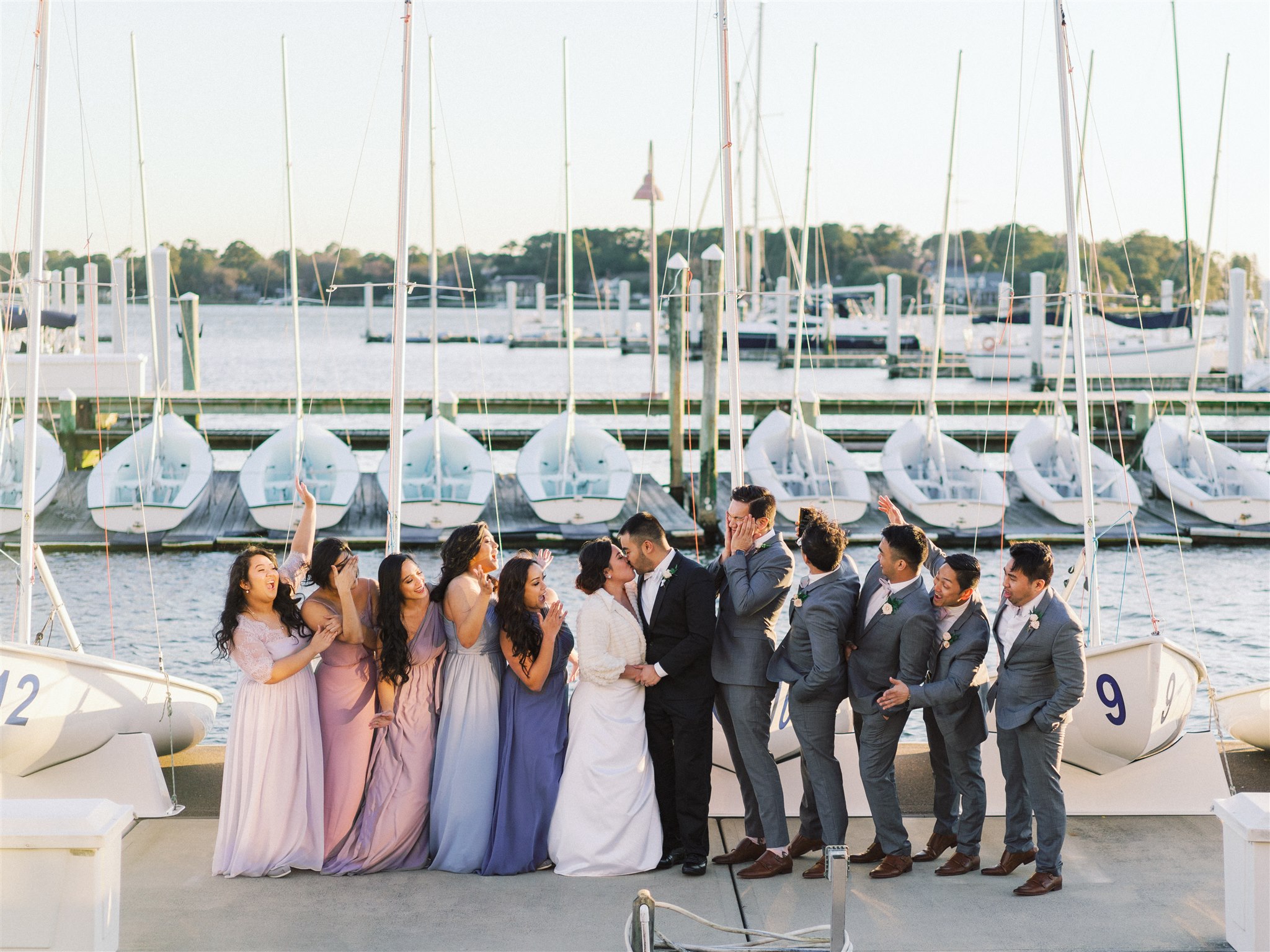 newlyweds kiss while bridal party cheers at Norfolk VA marina