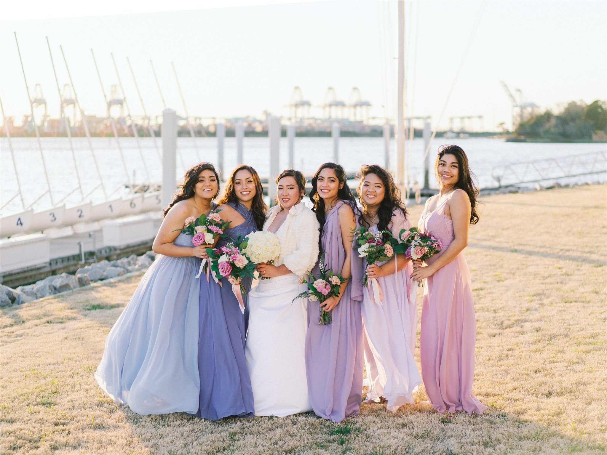 bridesmaids in pastel gowns stand on beach with bride