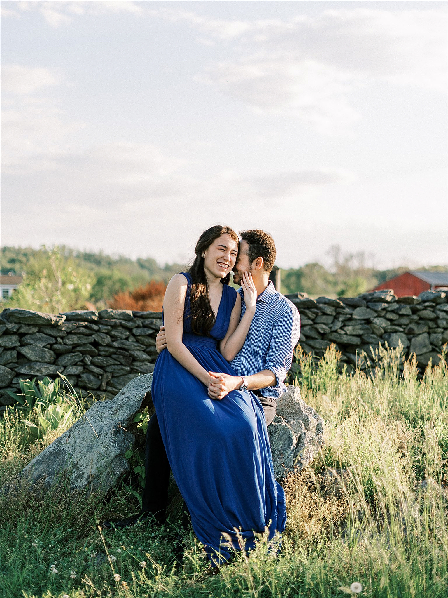 bride sits on groom's lap by stone wall at Goodstone Inn