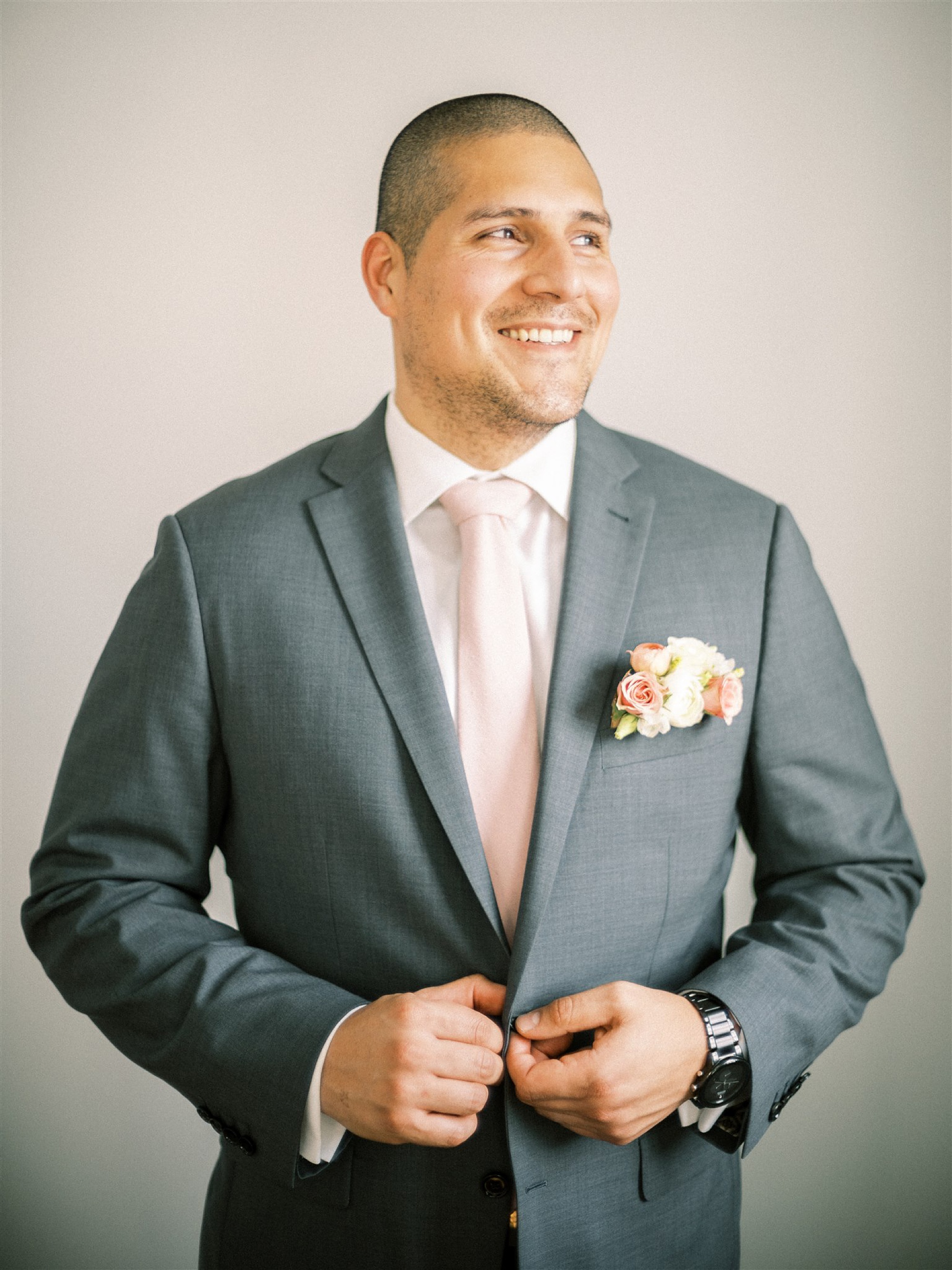 groom in grey suit and pink tie poses before wedding