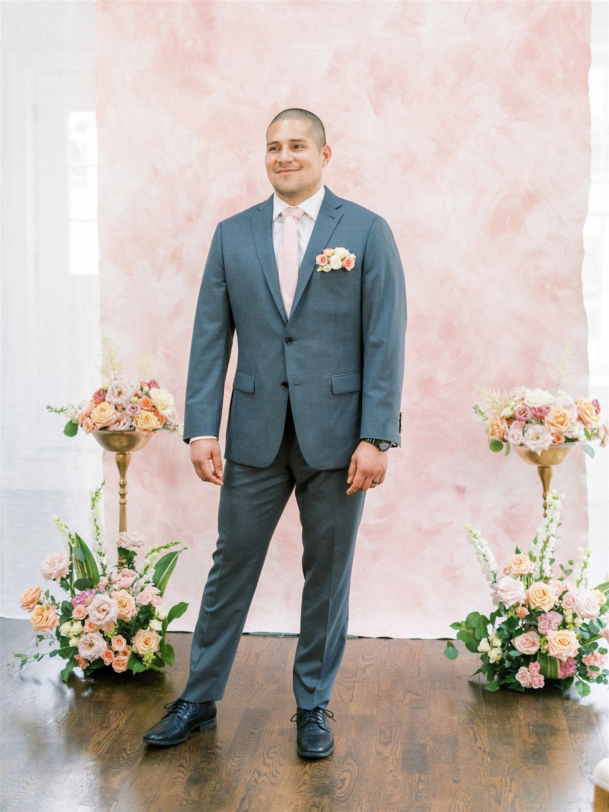 groom waits for bride at end of aisle with pink backdrop