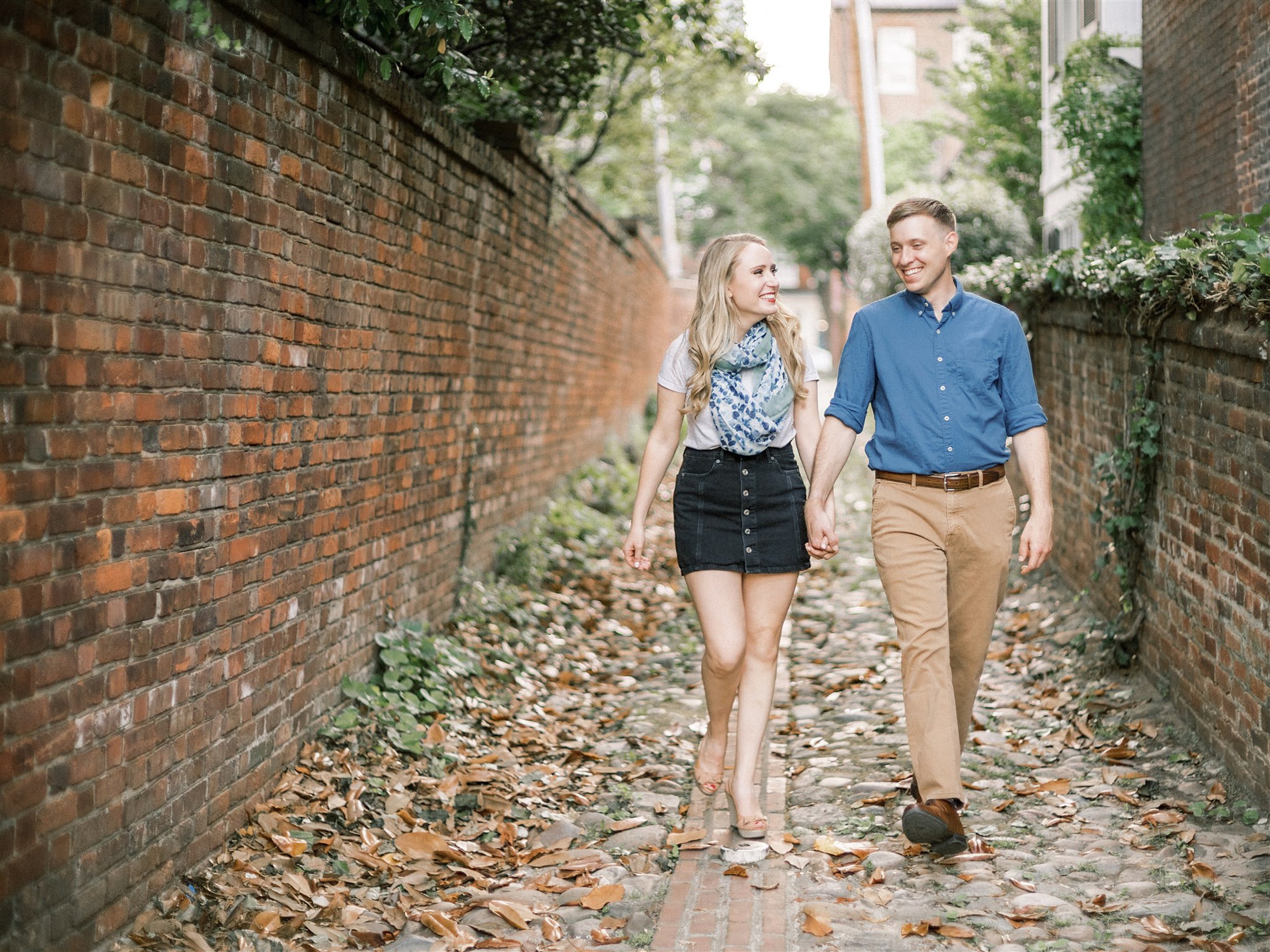 engaged couple walks on cobblestone road in Old Town Alexandria