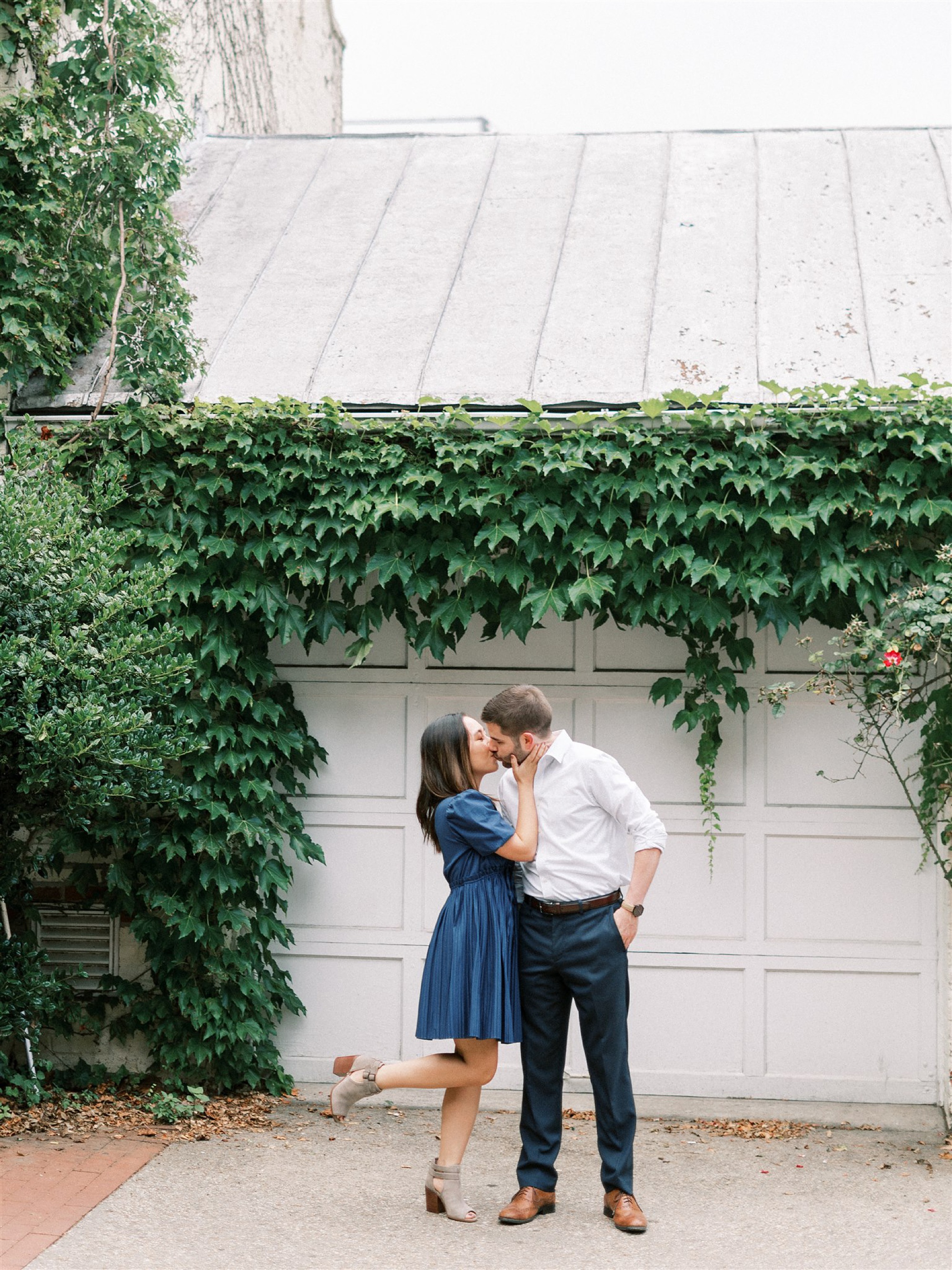 bride pops foot while kissing fiance in front of ivy covered wall