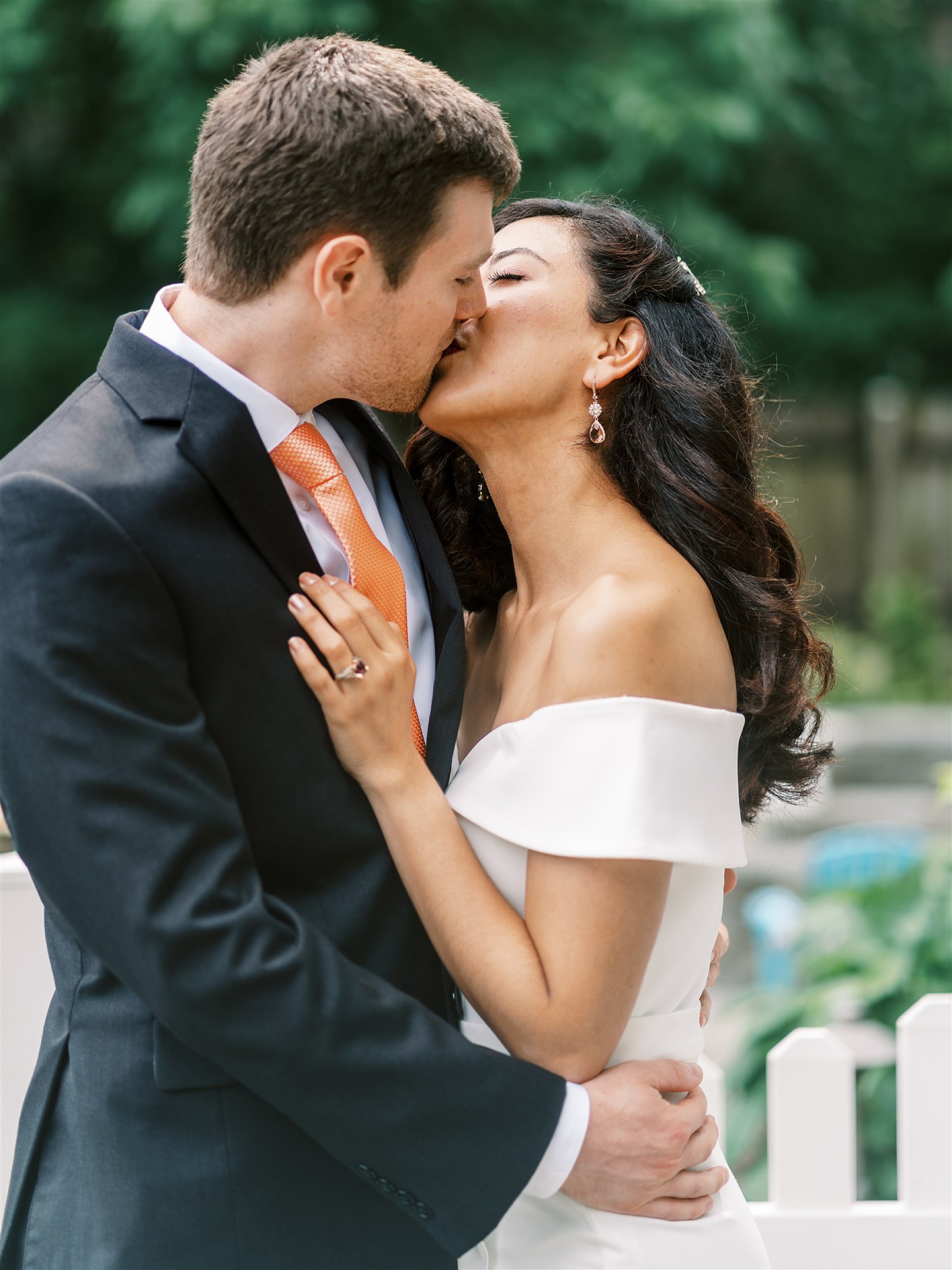 newlyweds kiss under white arbor in backyard 