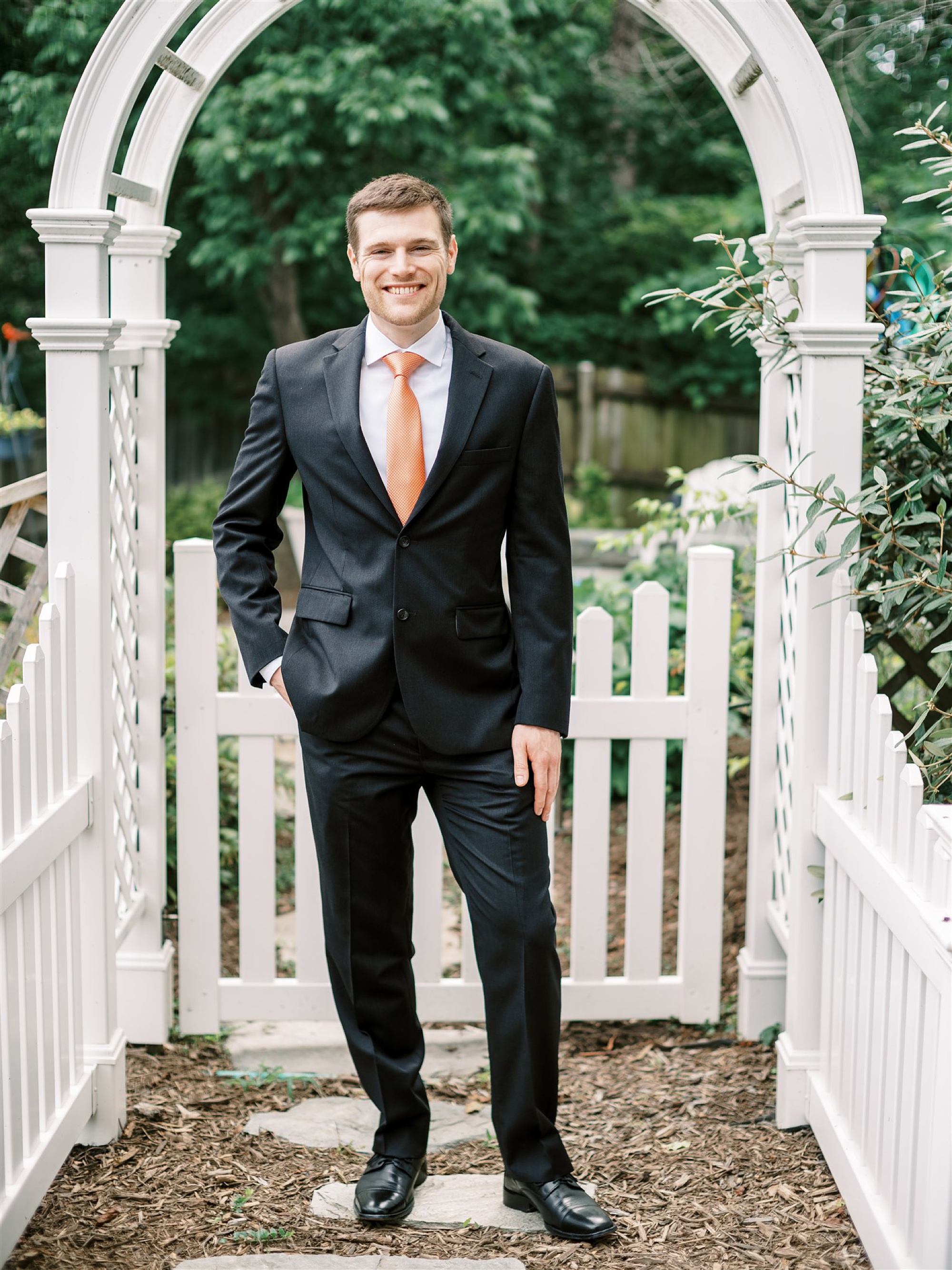 groom poses in suit with orange tie