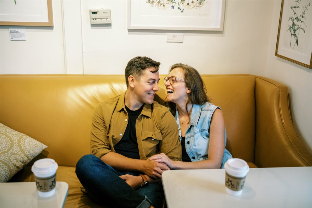 couple laughs on couch at Trinity House Cafe during engagement photos