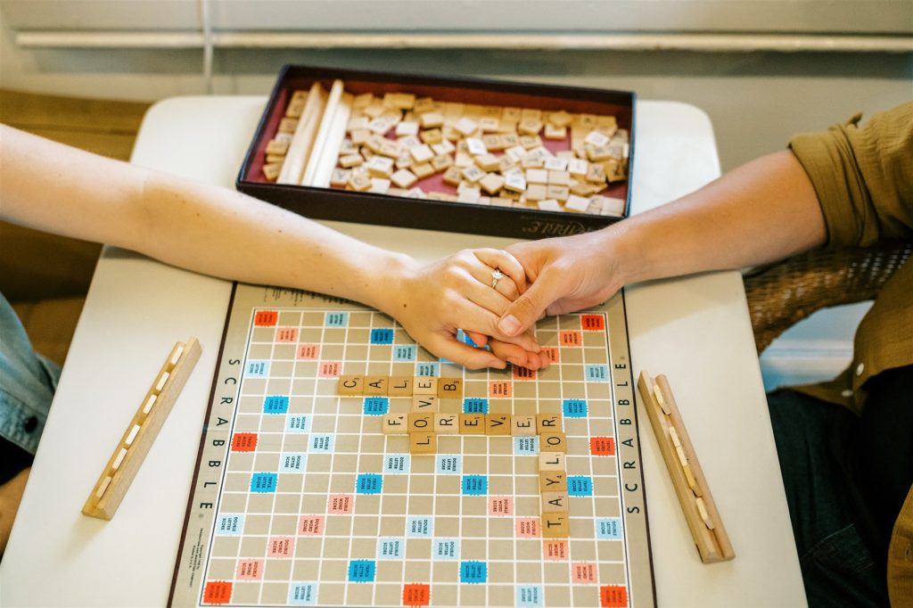 couple holds hands over Scrabble board during Trinity House Cafe engagement photos
