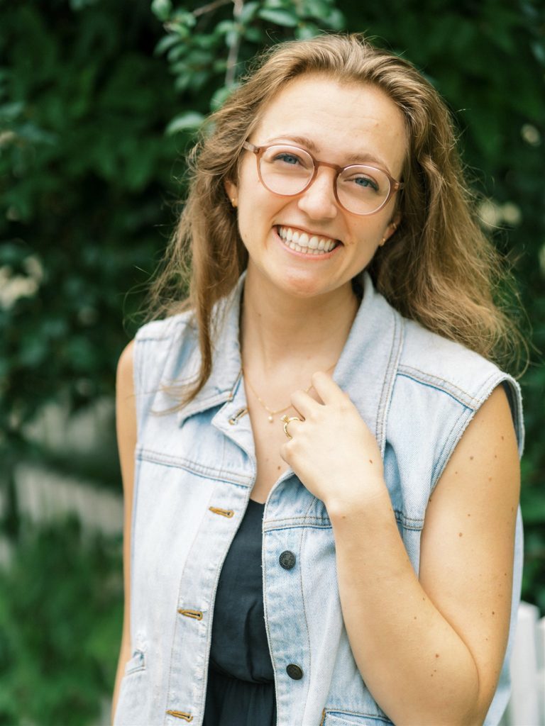 bride in jean jacket holds onto necklace showing off engagement ring 