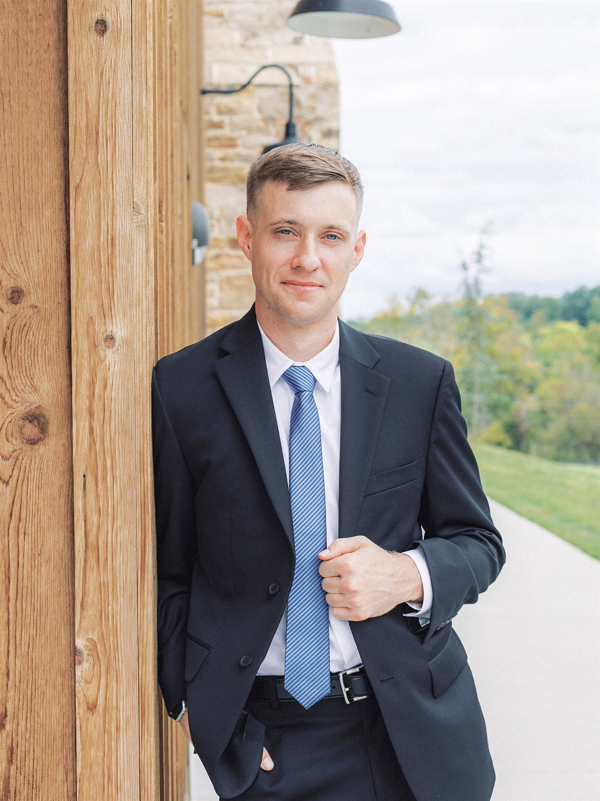 groom in black suit with blue tie poses at Mt Defiance Cidery