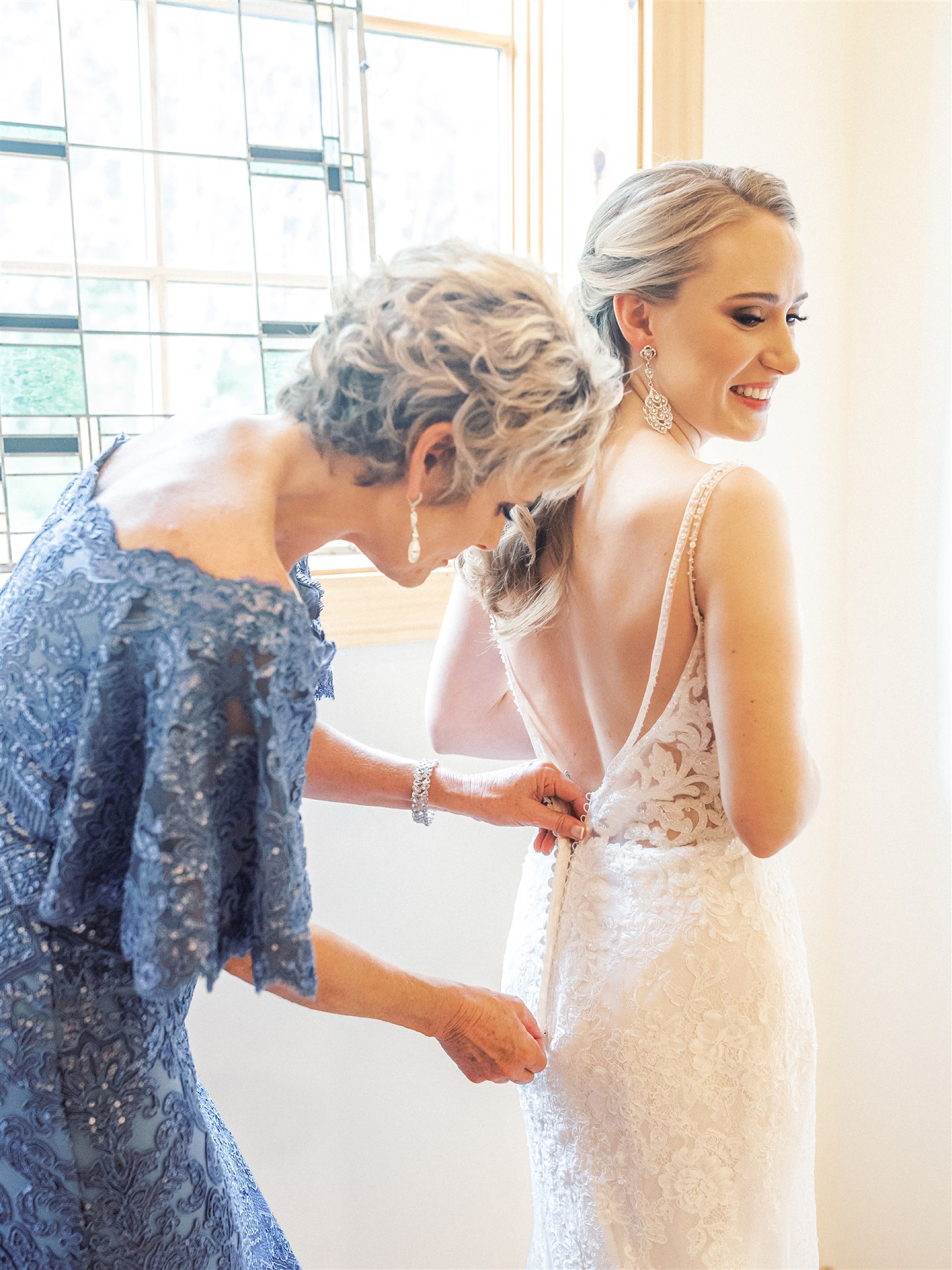 mother of bride helps bride with wedding gown