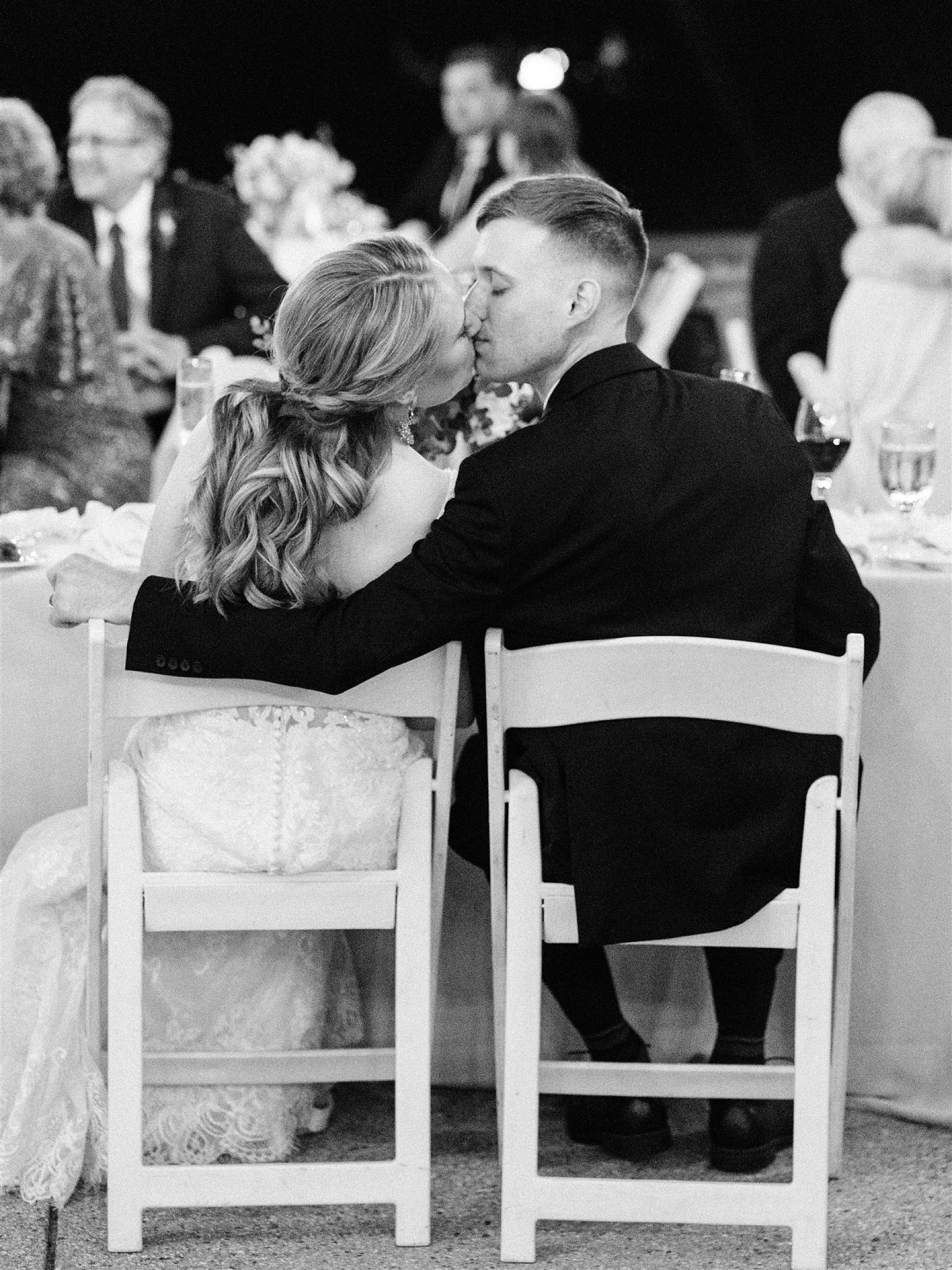 groom kisses bride sitting at sweetheart table