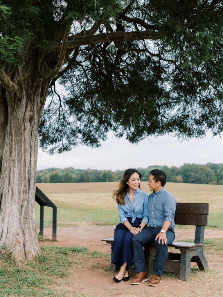 engaged couple sits on bench during Manassas Battlefield Park engagement session