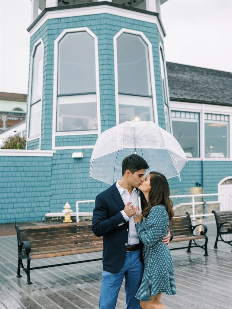 engaged couple kisses under umbrella by blue building