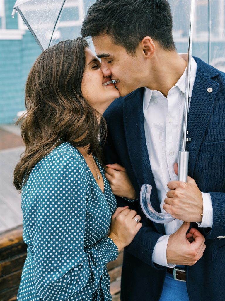 engaged couple kisses under clear umbrella during rainy engagement in Old Town Alexandria