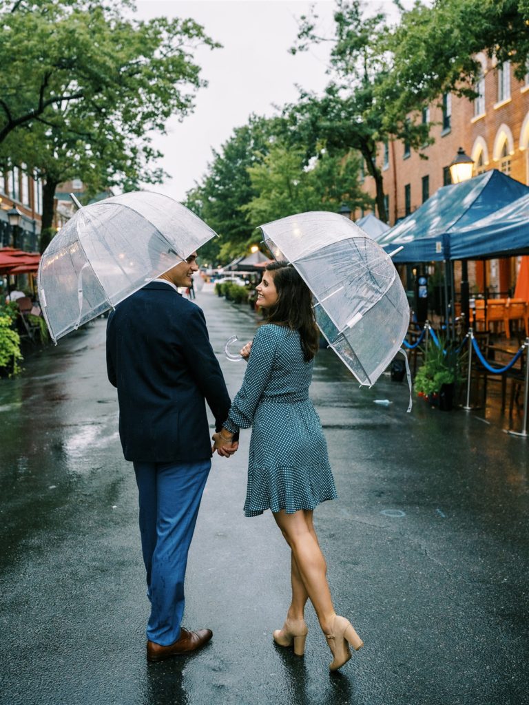 engaged couple walks down street in Old Town Alexandria during rain fall