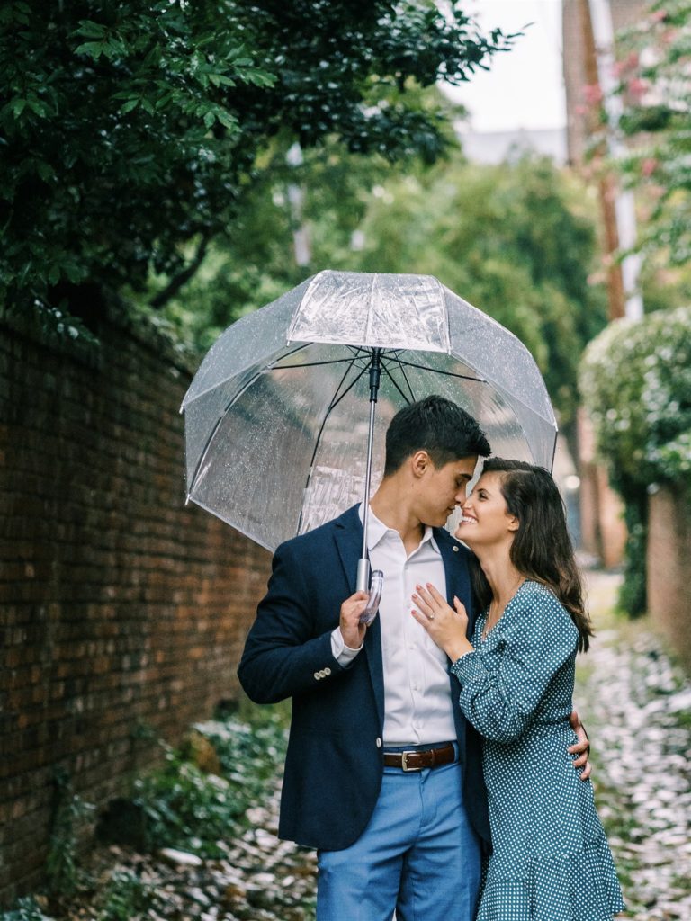 groom hugs fiancee to side under umbrella in Old Town Alexandria