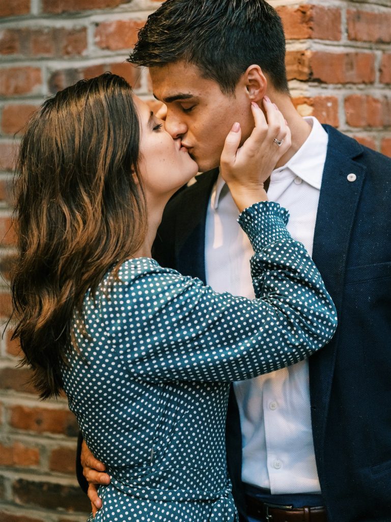couple kisses by brick building in Old Town Alexandria during engagement photos 