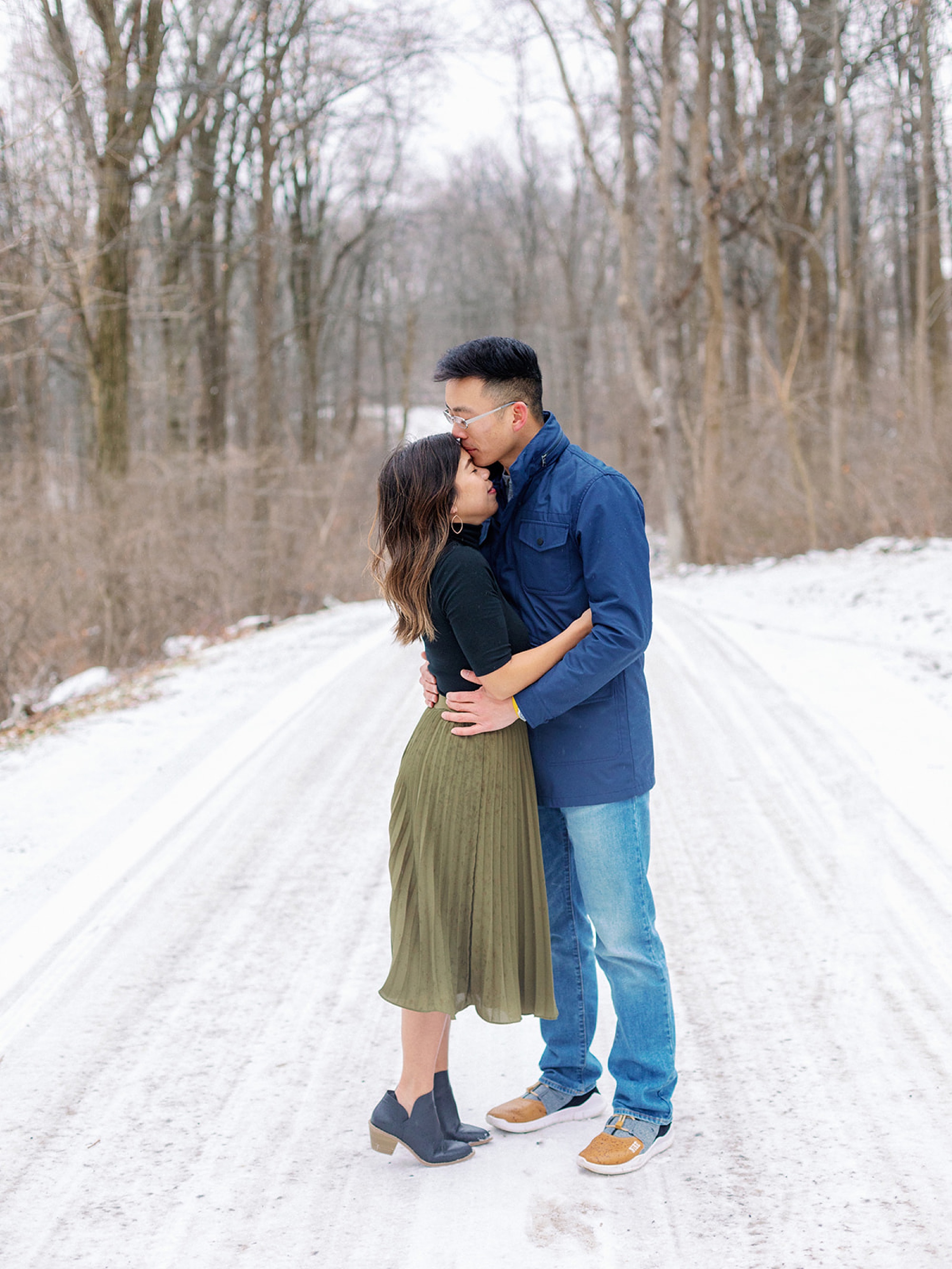 groom kisses bride's forehead standing in the snow